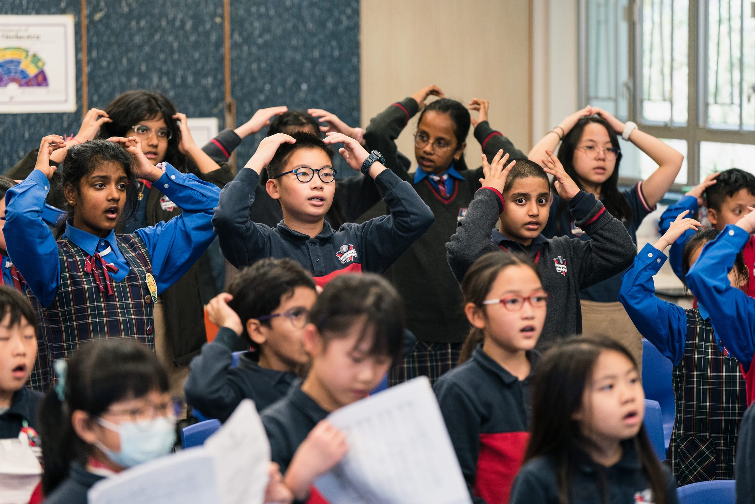 Primary school students singing with their hands on their heads during an HKVC classroom choral activity